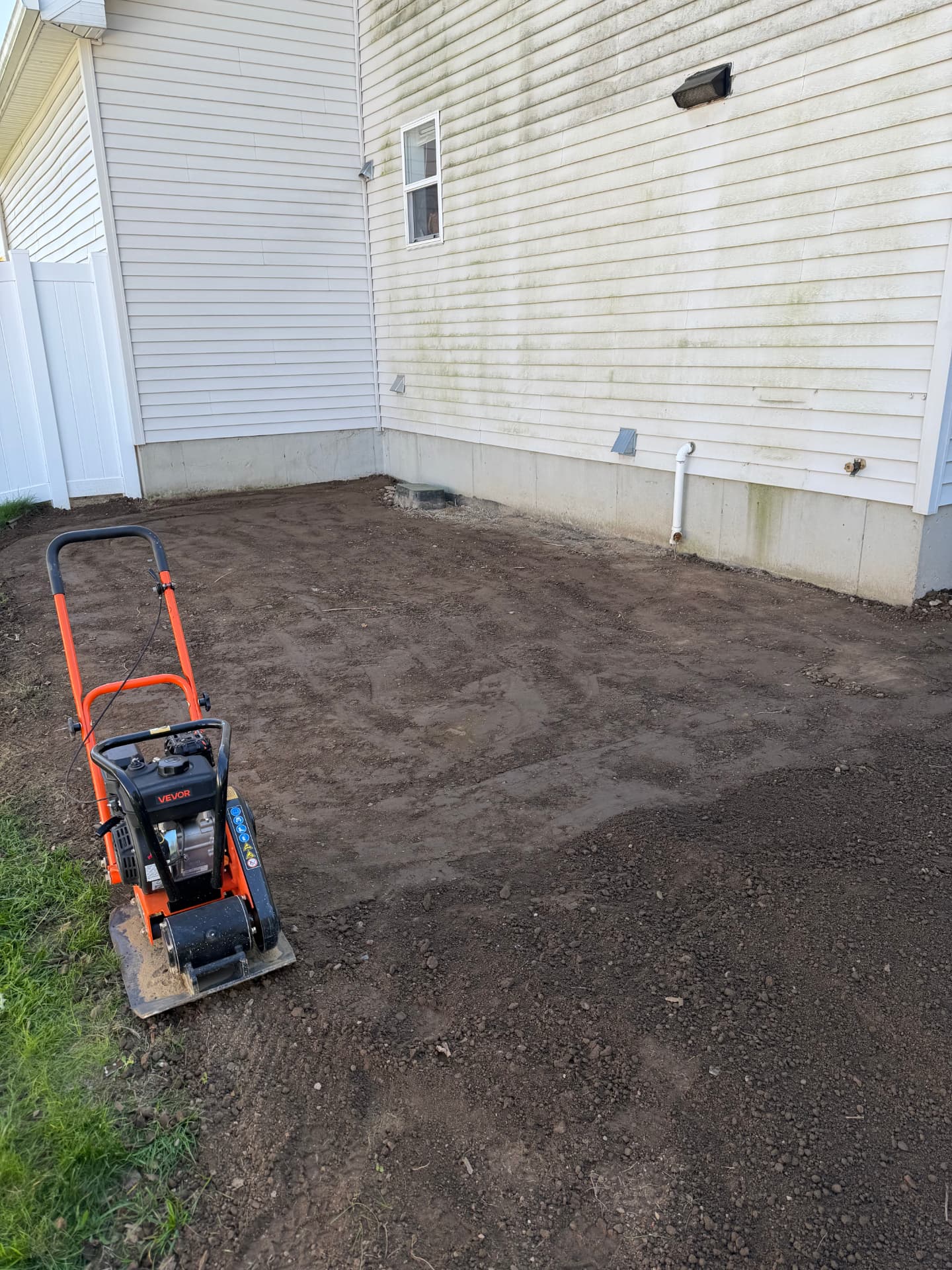 Plate compactor on soil beside a foundation